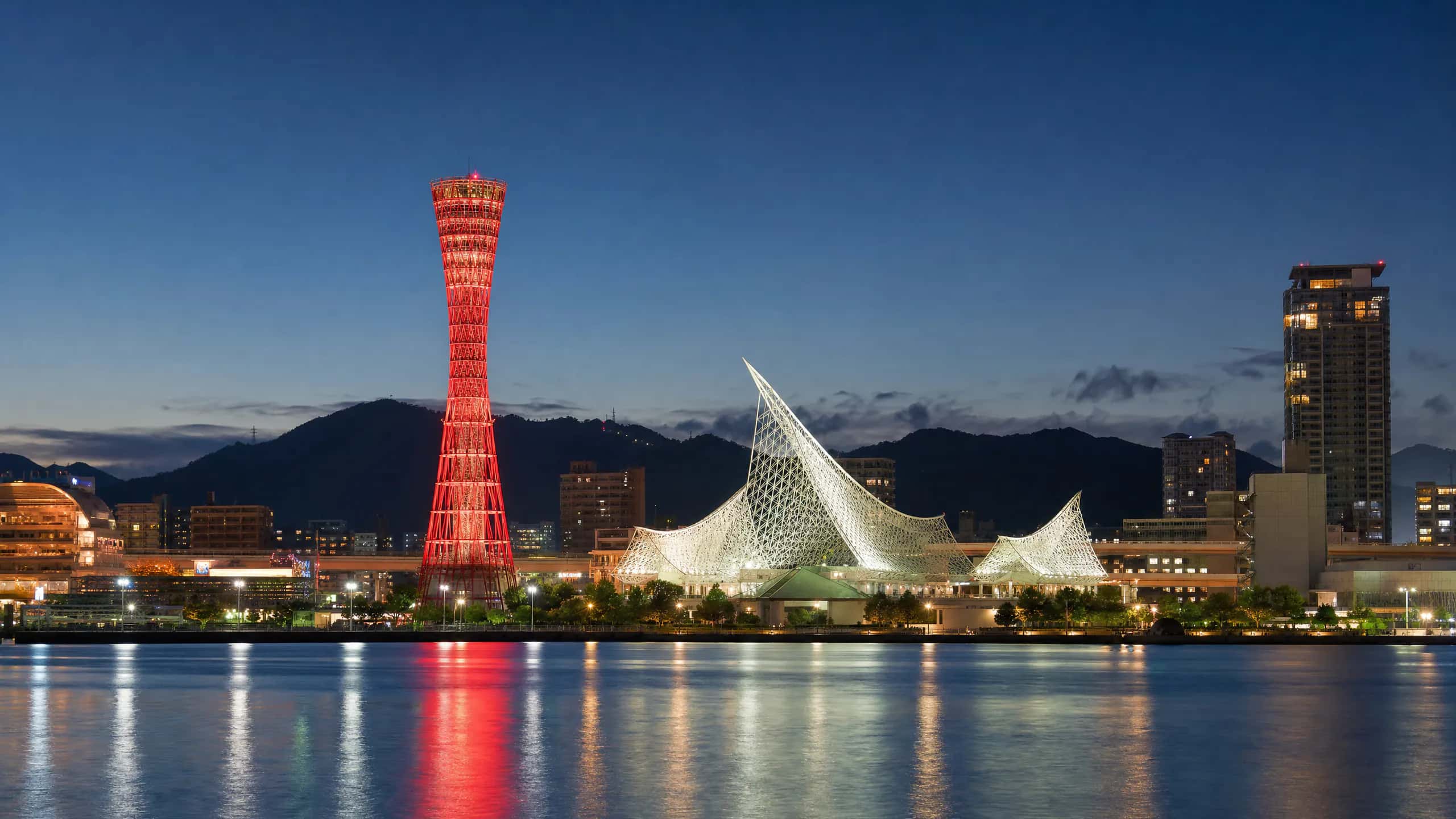 夕暮れの神戸港。ライトアップされたポートタワーと海洋博物館、背後に六甲山