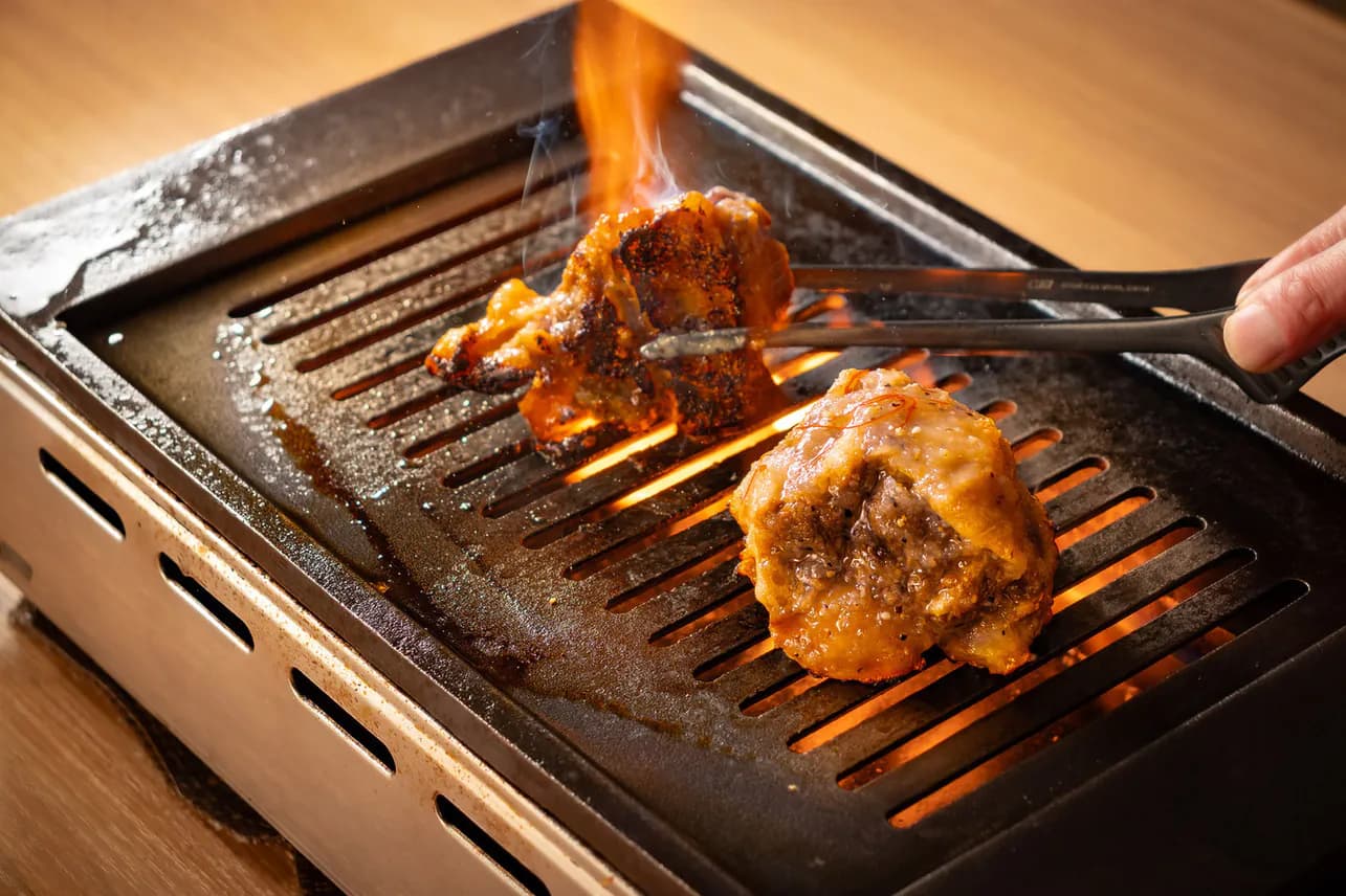 炎が上がる焼き台でトングを使う手元